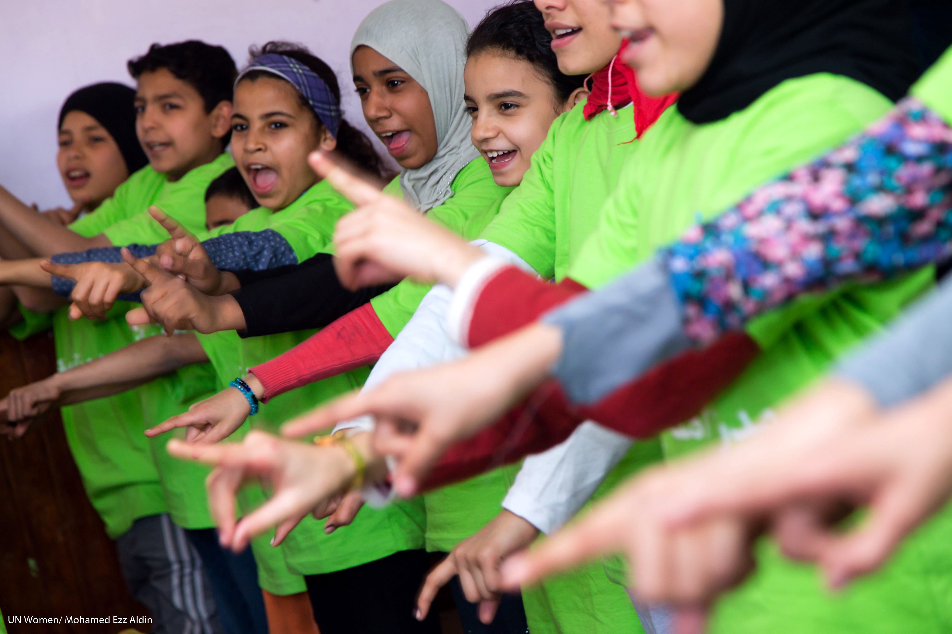 Kinder in Ägypten singen während einer Sensibilisierungskampagne zur Beendigung von Gewalt gegen Frauen. Die Kinder stehen in einer Reihe und halten ihre ausgestreckten Zeigefinger nach vorn.