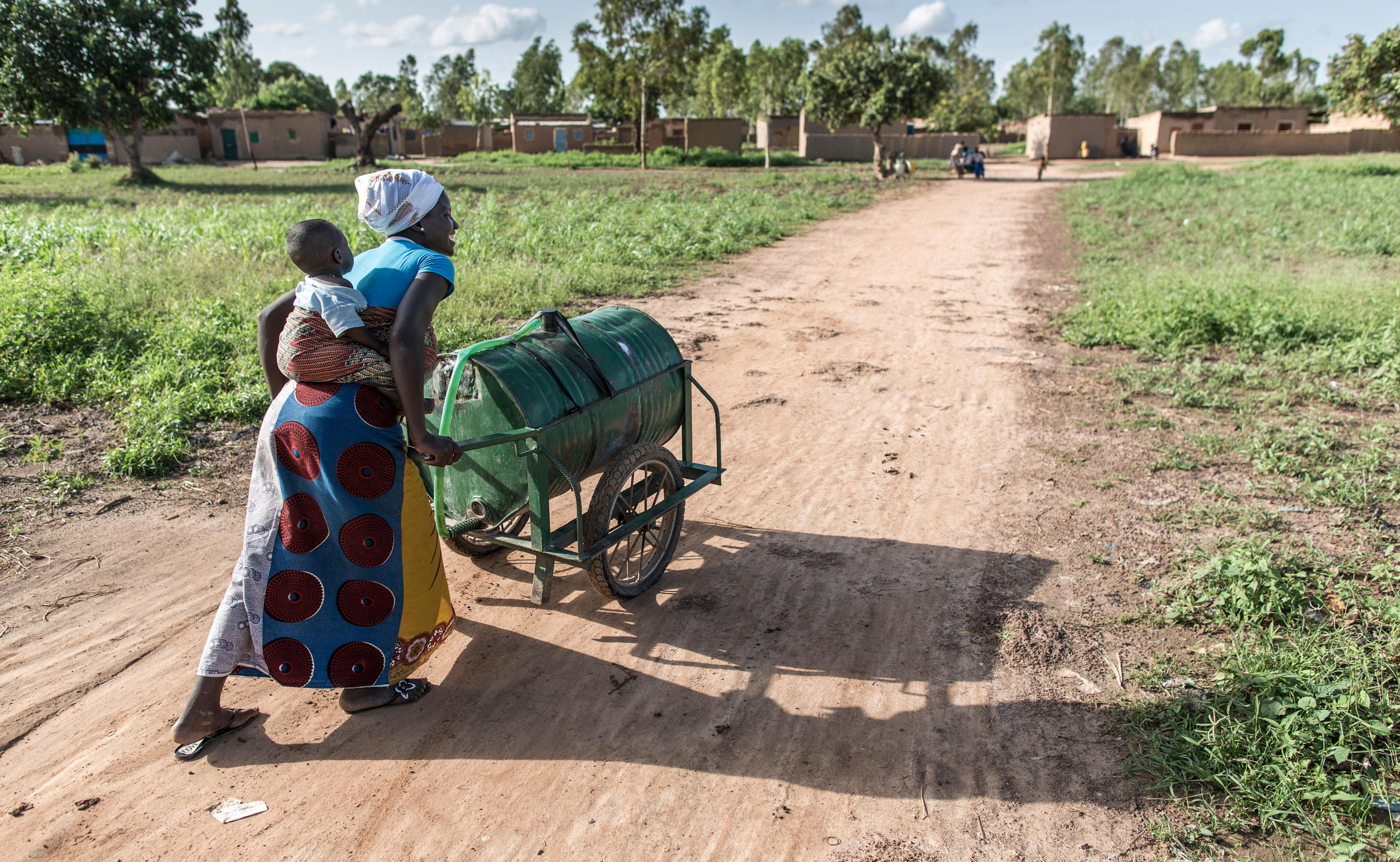 Eine Frau schiebt einen Trinkwassertank, den sie an einer öffentliche Wasserzapfstelle in Ouagadougu, Burkina Faso, befüllt hat.